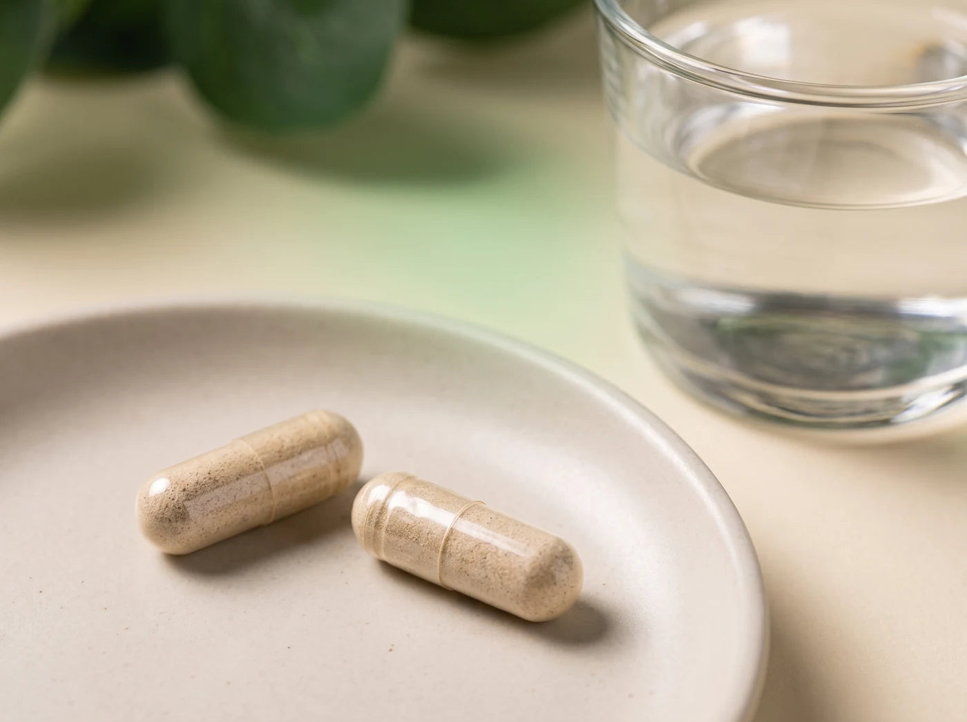 Two tan capsules on a ceramic dish beside a glass of water; illustrative image